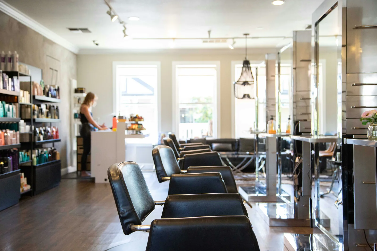 A hair salon interior with a row of styling chairs and mirrors, and a team member working at the reception desk.