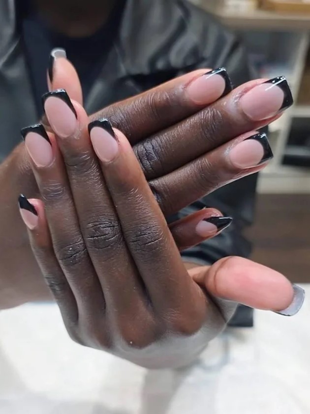 woman in a nail salon showing her nude BIAB manicure with black extensions to the camera