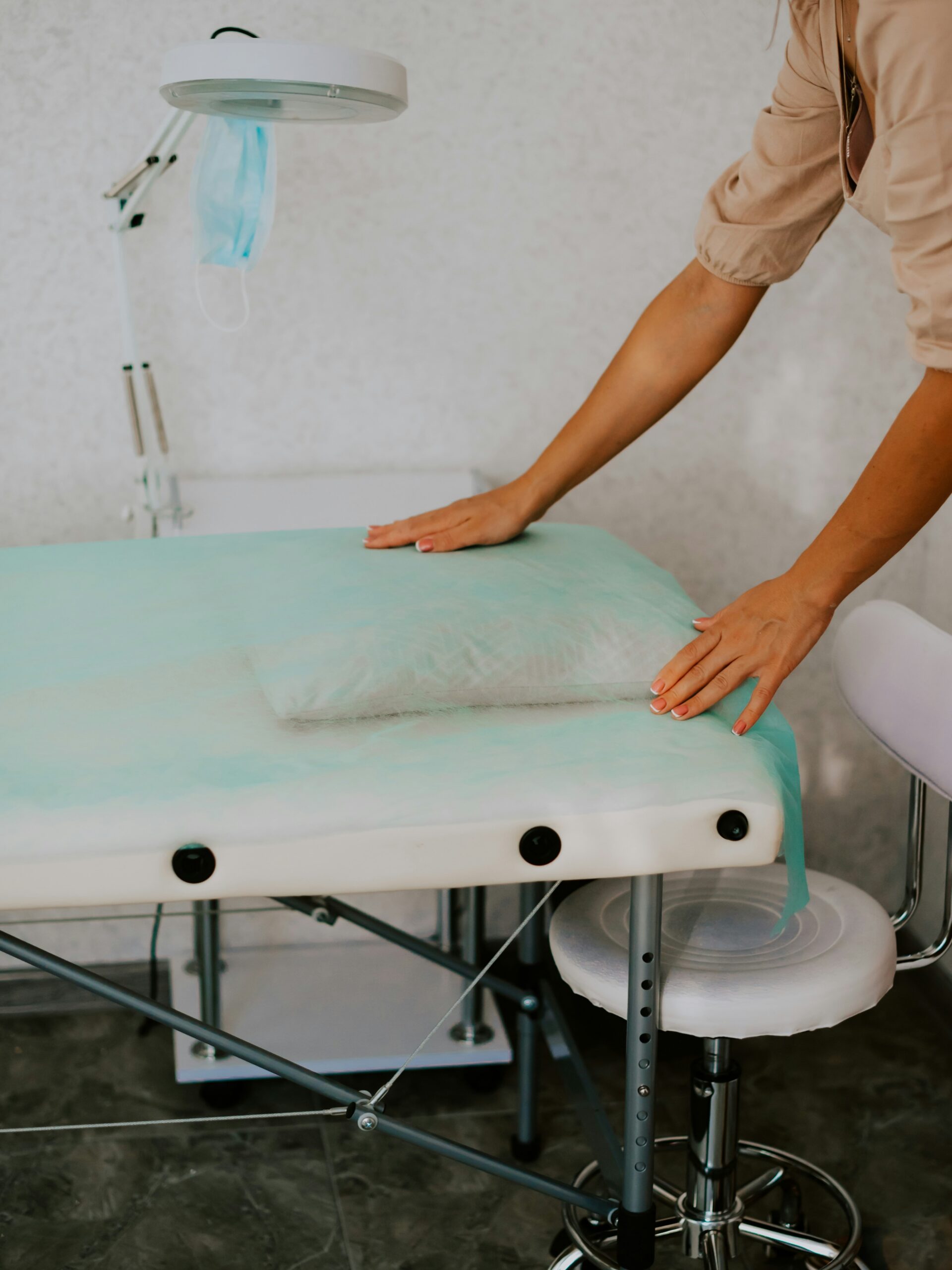 A beauty salon treatment room showing a clean, hygienic space and a technician laying a clean sheet of paper over a treatment bed