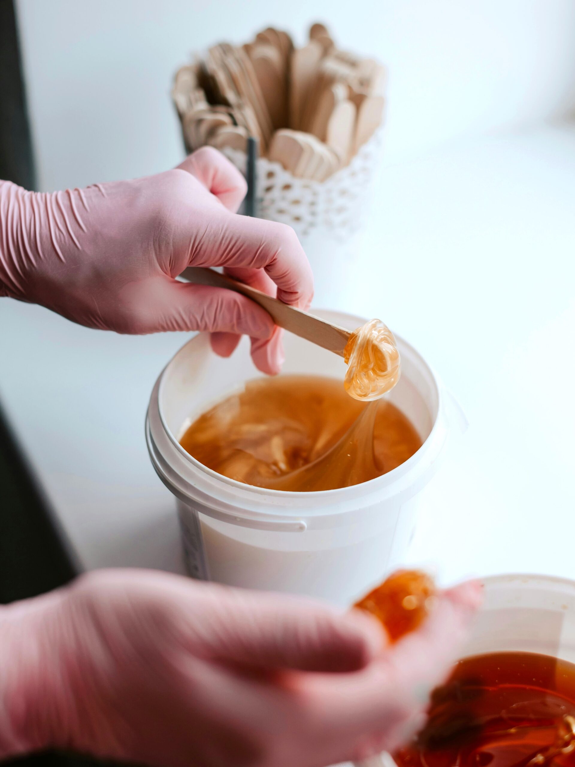 Close-up of two pots of sugar wax with a practitioner scooping some wax using a spatula