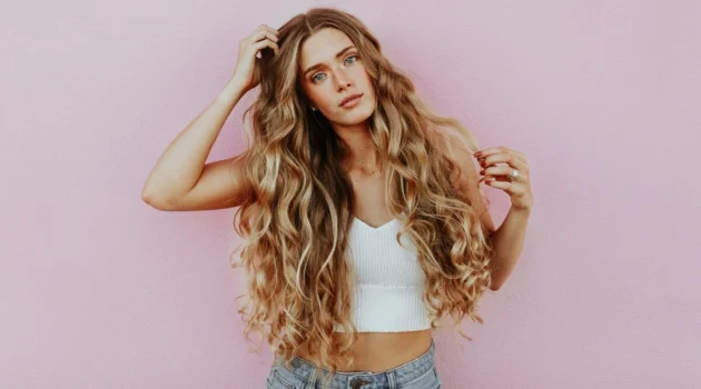 Studio shot of woman with very long, wavy, sun-kissed balayage hair wearing light blue jeans and a white knitted crop top