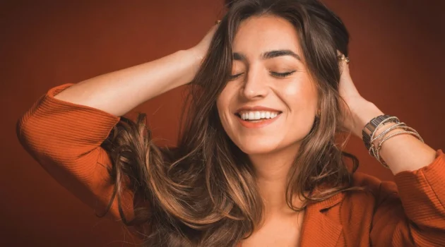 Close-up of woman smiling with her eyes closed and running her hands through her soft long brunette hair