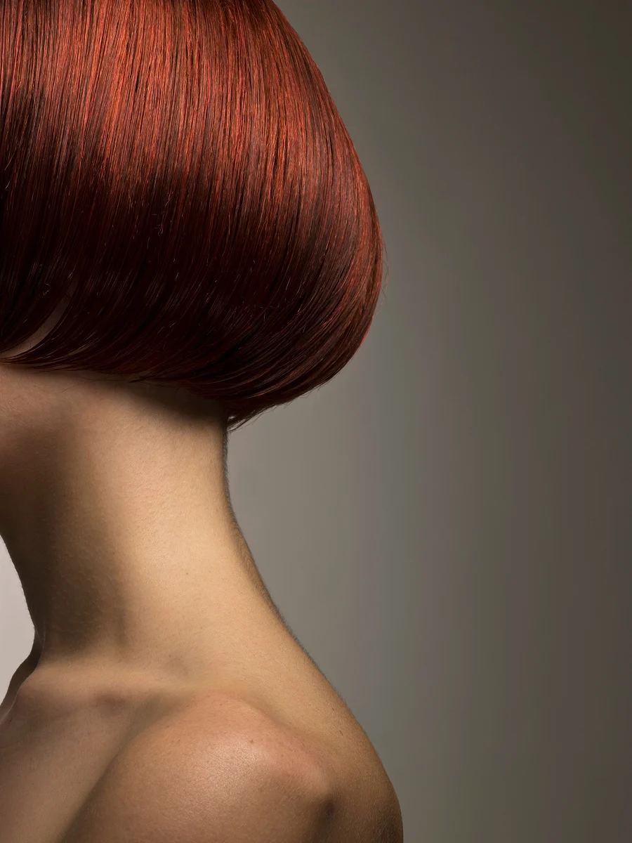 Close-up side view of a woman’s head showing a glossy dyed red bob