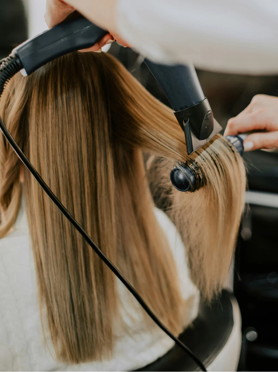 Back view of a woman at a hairdressers as a stylist dries her hair straight during a keratin treatment appointment