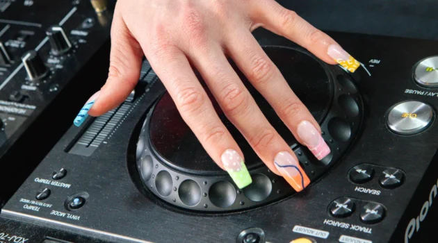 A hand wearing the electric mani on a Pioneer DJ jog wheel, neon French tips in animal print and swirls