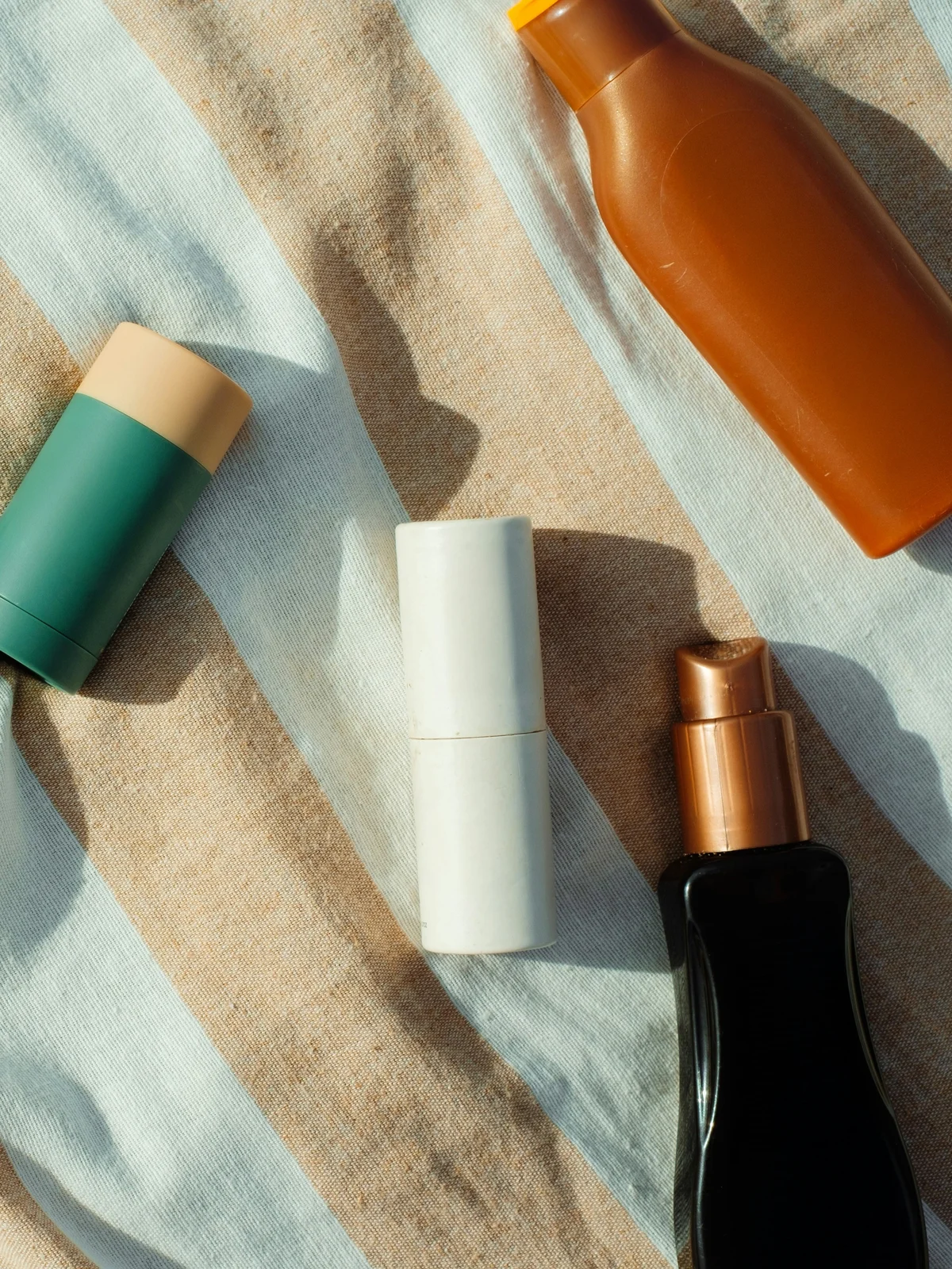 Top view of small bottles and tubes of skincare products resting on a striped cotton fabric