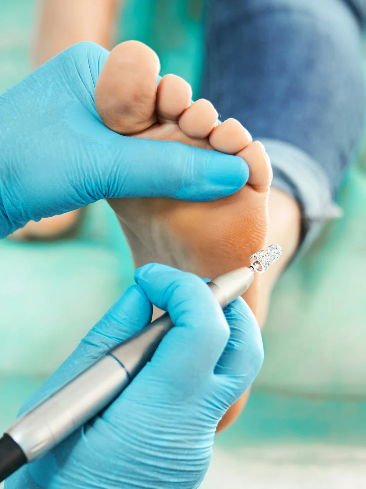 Close-up of a technician with a gloved hand using a small electric file to gently exfoliate a client’s foot
