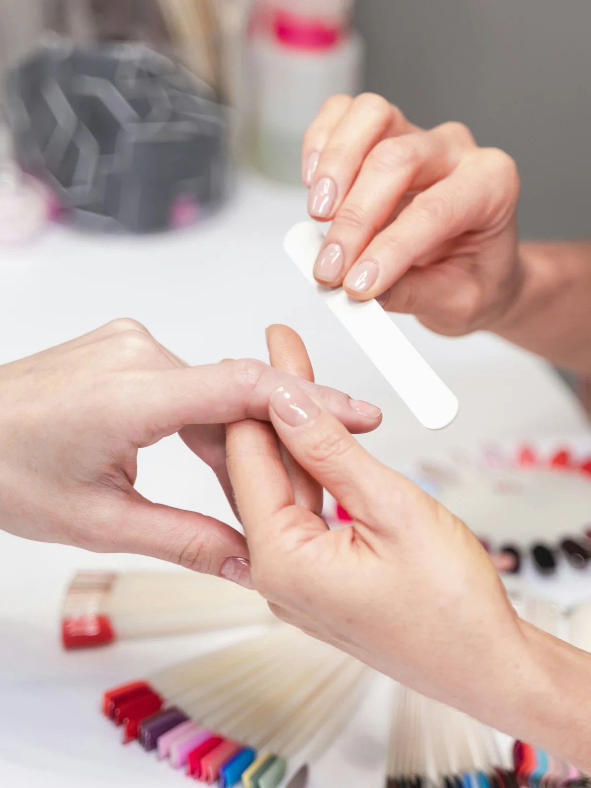 Close-up of a technician gently filing a client's nails in a beauty salon with manicure products and equipment in the background