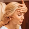 Close-up of a woman with her eyes closed as a therapist holds one hand on her forehead and massages her neck with the other hand during an Indian head massage