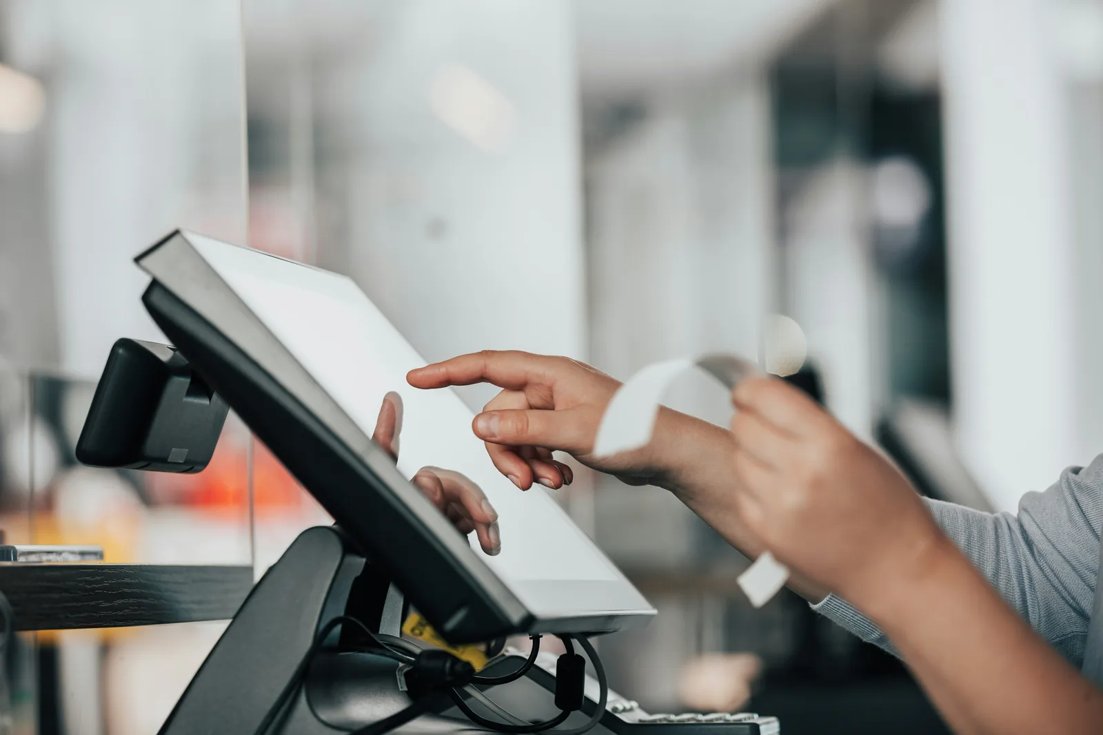 Des mains utilisent une caisse tactile au comptoir et détachent un ticket imprimé