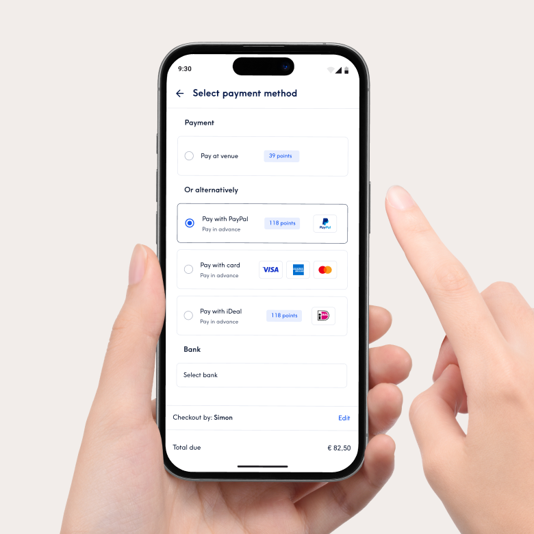 Close-up van een smartphone met de betaalinterface van de Treatwell-app om een betaalmethode te selecteren. Opties zijn onder meer betalen in de salon of vooraf betalen met PayPal, kaart of iDeal. Een hand houdt de telefoon vast en een vinger wijst naar het scherm.