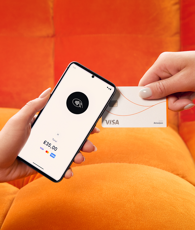 Een hand houdt een smartphone vast die fungeert als betaalterminal, met een icoon voor contactloos betalen en een totaal van £35,00, terwijl een andere hand een witte Visa-creditcard ertegenaan houdt om te betalen. De achtergrond is een feloranje bank.
