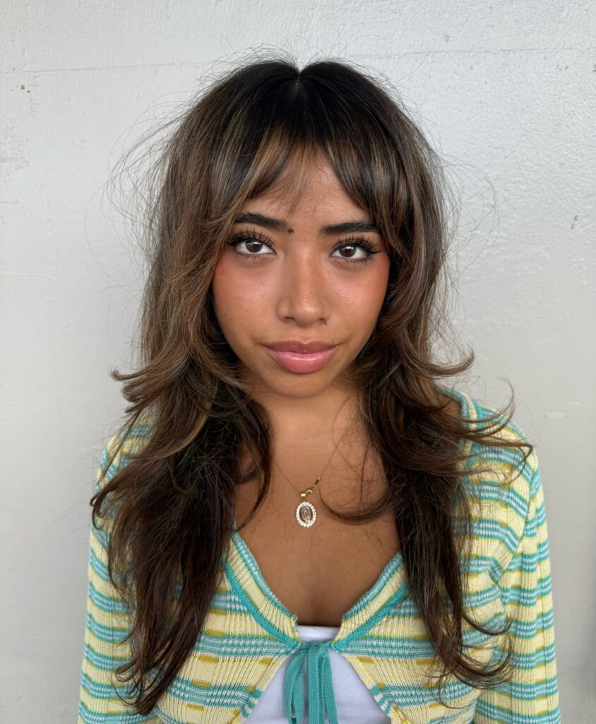 A woman with long brown hair styled with curtain bangs parted down the middle and swept to the sides for a classic face-framing look.