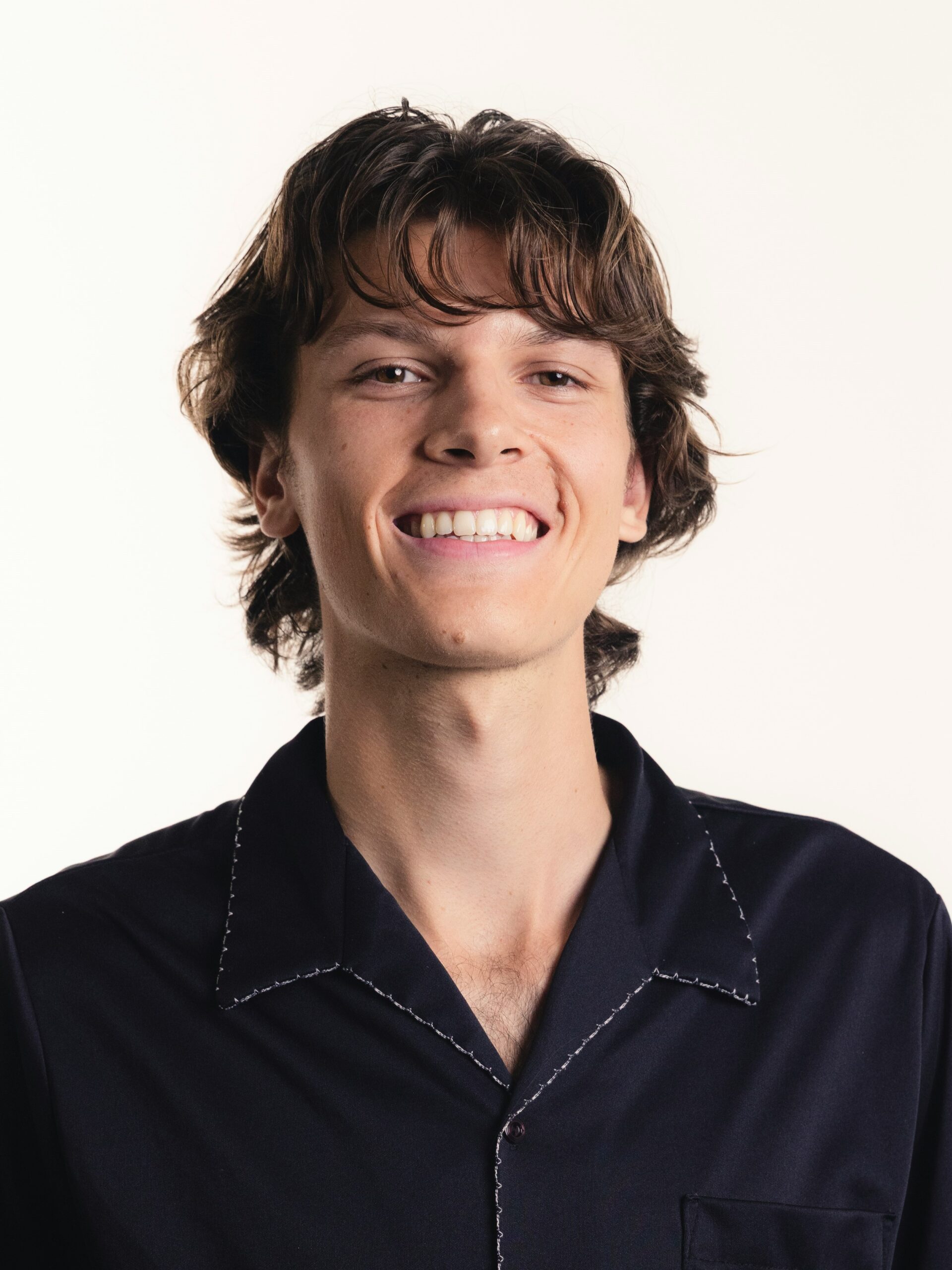 Un jeune homme avec un mulet texturé et dégradé, portant une chemise bleu foncé, souriant.