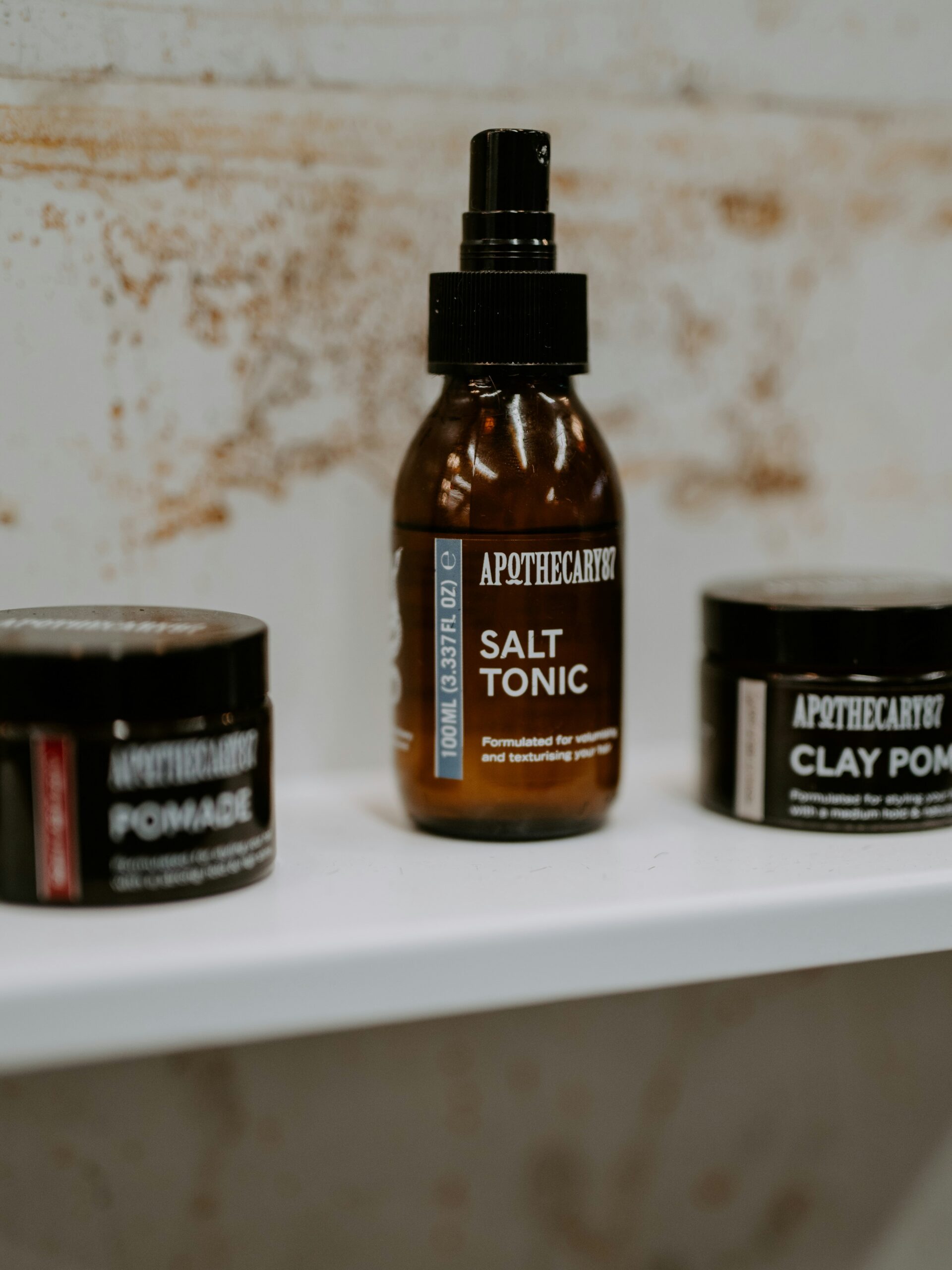 Une gamme de produits coiffants pour mulet dans des contenants marron, disposés sur une étagère blanche.