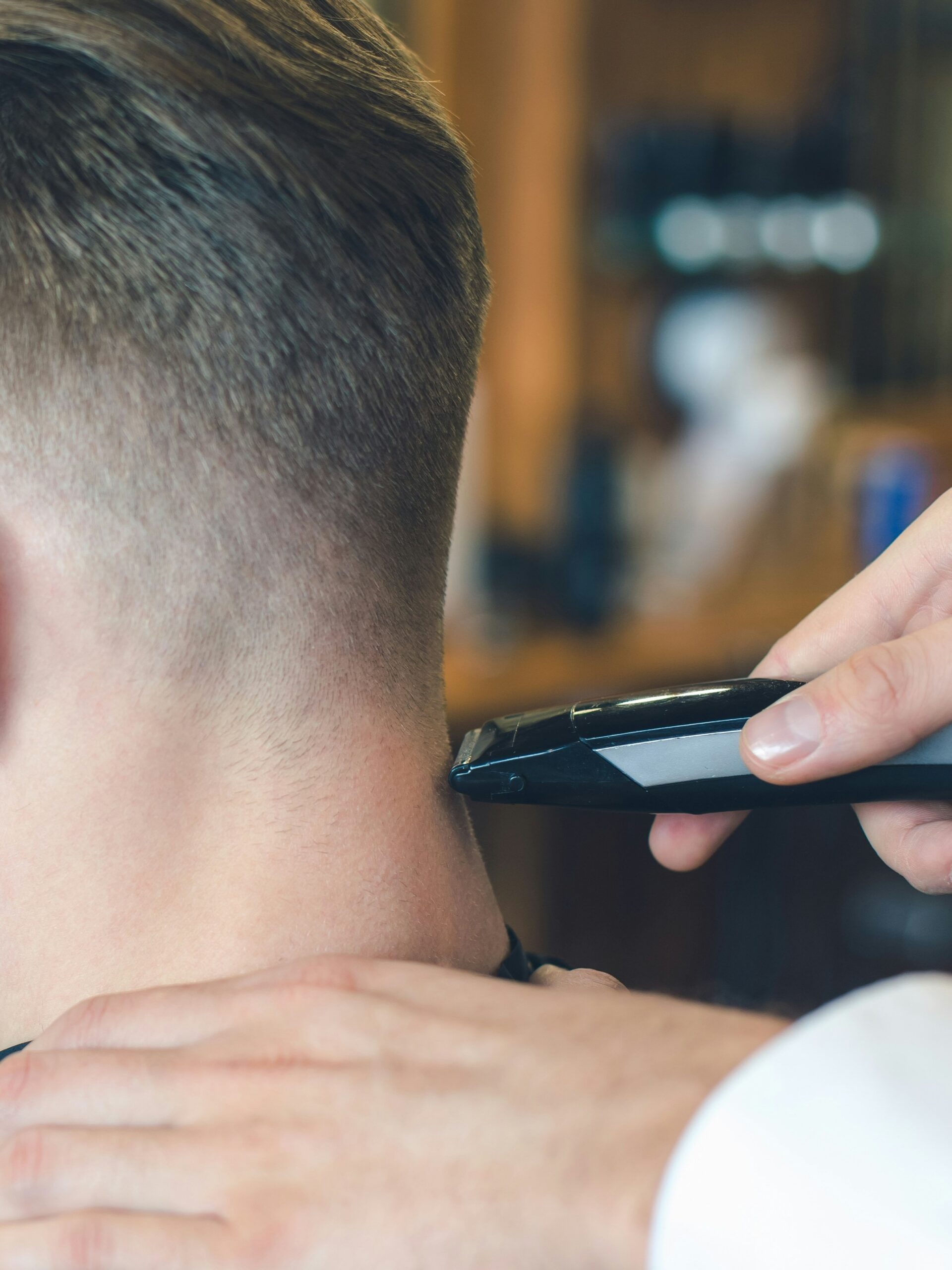 Gros plan d'un coiffeur réalisant un taper fade sur un client aux cheveux raides avec une tondeuse à l'arrière de la tête