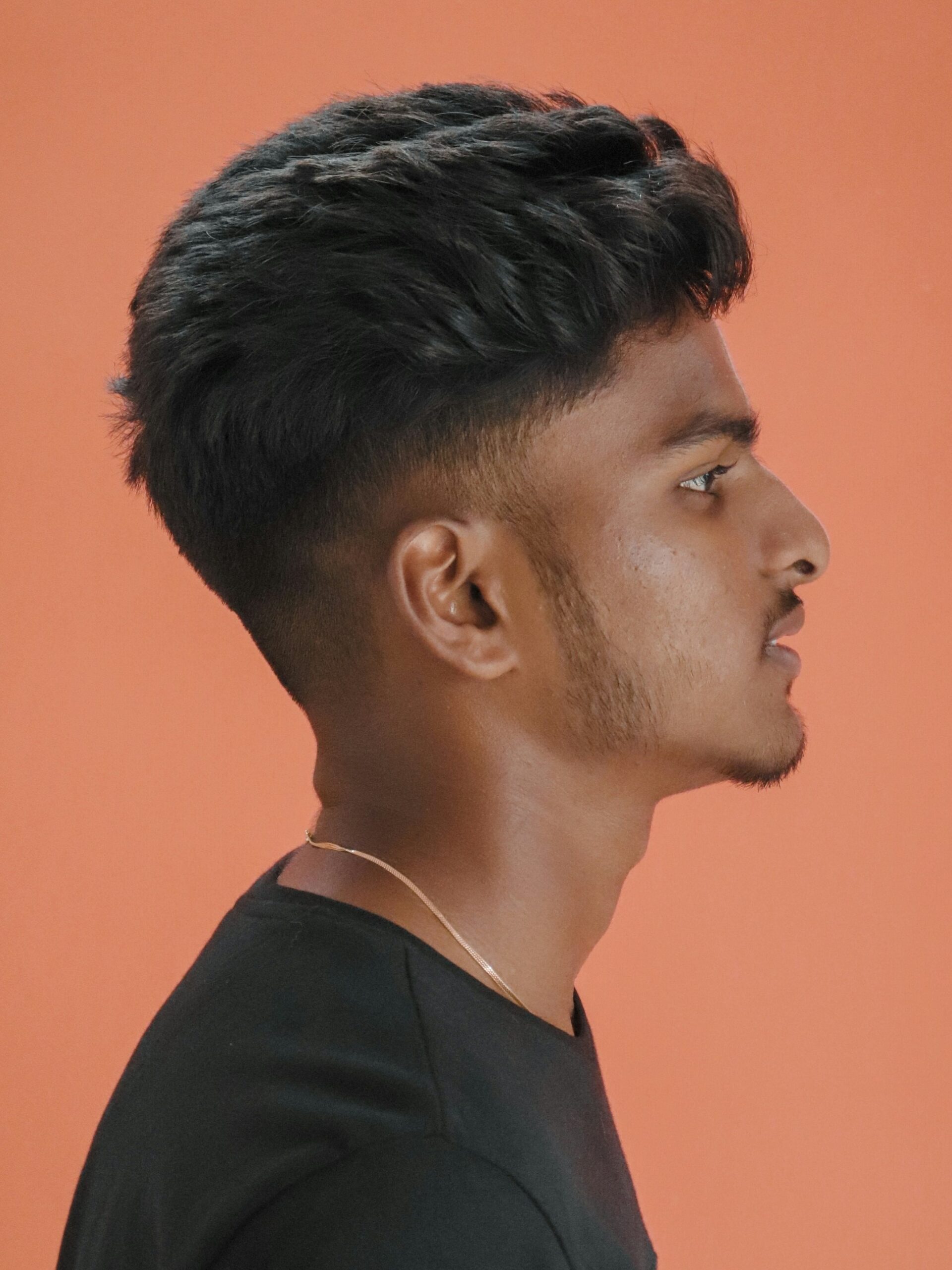 Portrait de profil d'un homme avec une coiffure volumineuse et texturée associée à un taper fade bas