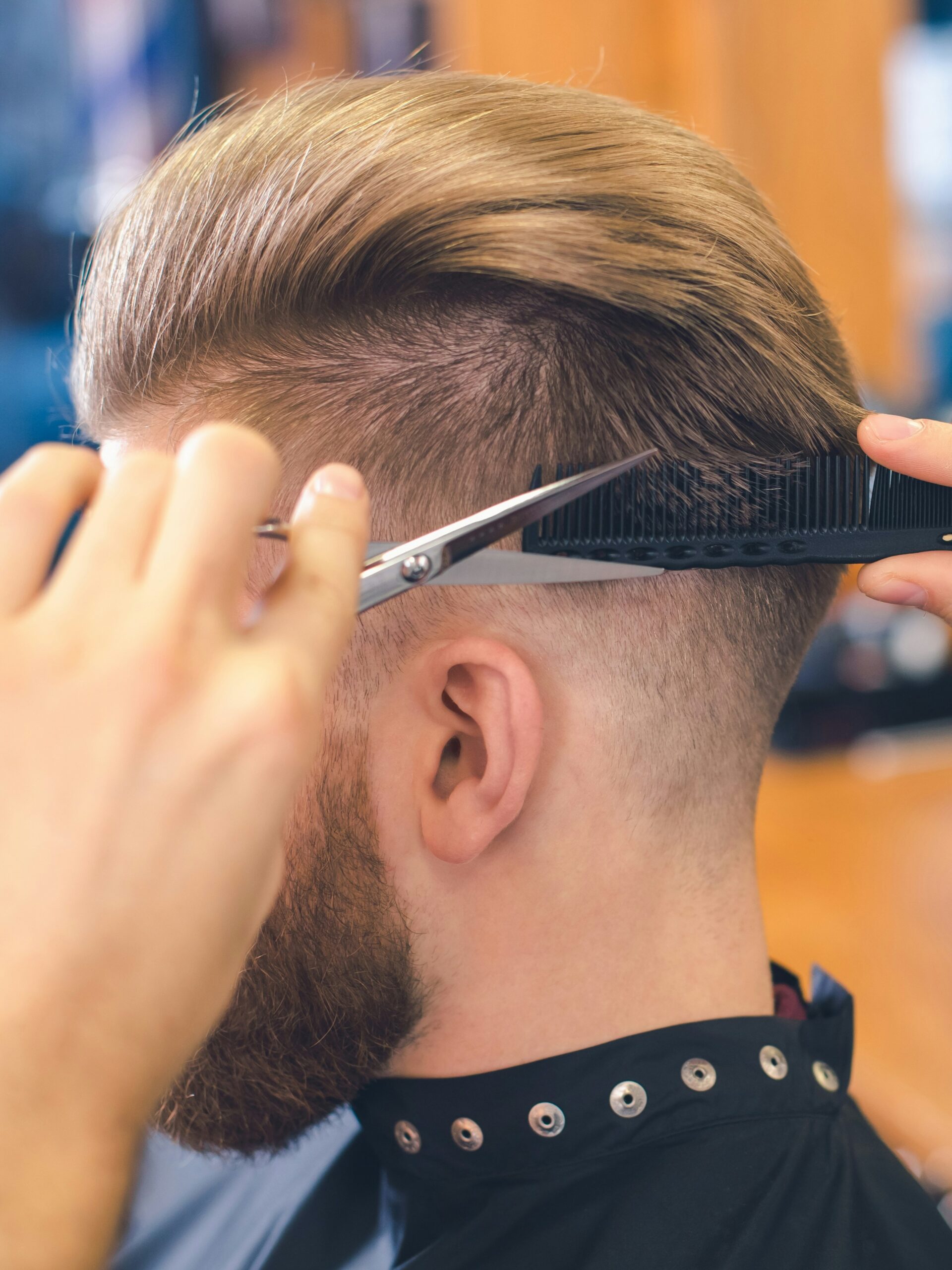 Gros plan d'un coiffeur réalisant un taper fade avec la technique ciseaux sur peigne à l'arrière de la tête du client