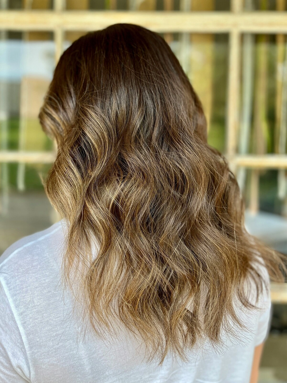 Vue de dos de la tête d'une femme montrant un balayage ondulé où les cheveux foncés se fondent dans des tons chauds