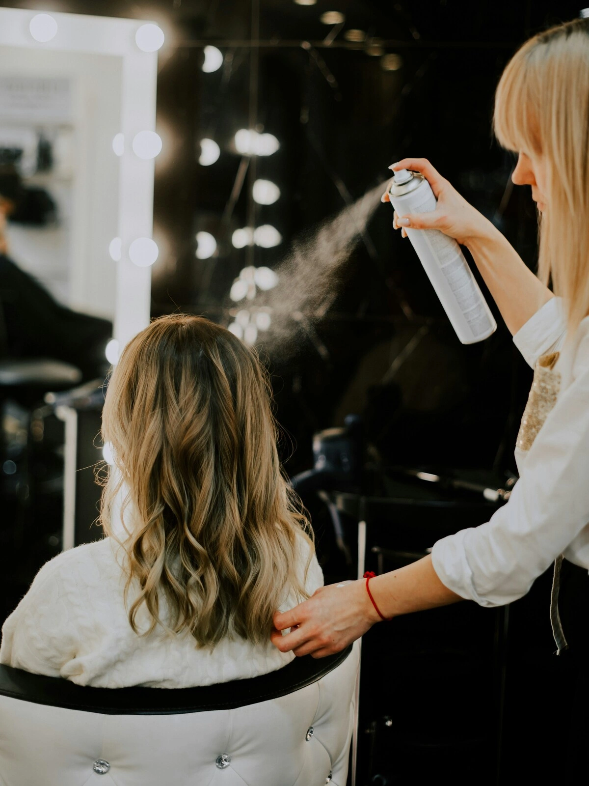 Une coiffeuse vaporise un produit de finition sur les cheveux d'une cliente après un balayage, un brushing et une mise en forme en vagues