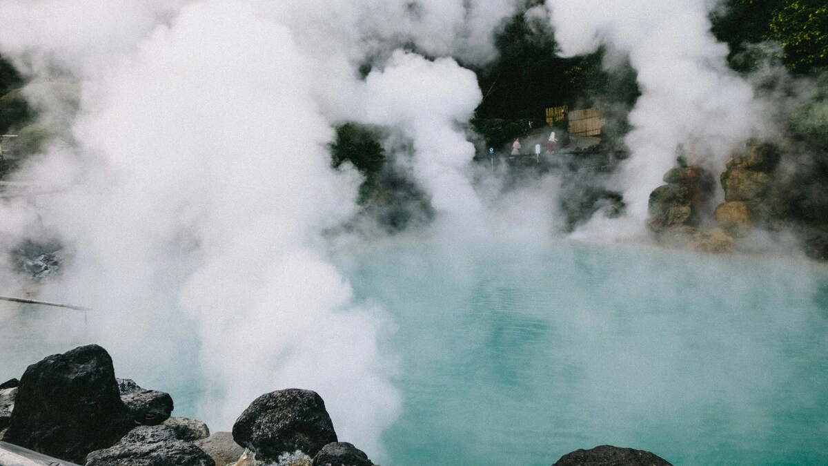 Vue large de sources chaudes au Japon, avec des nuages de vapeur s'élevant d'un bassin entouré de rochers et de verdure