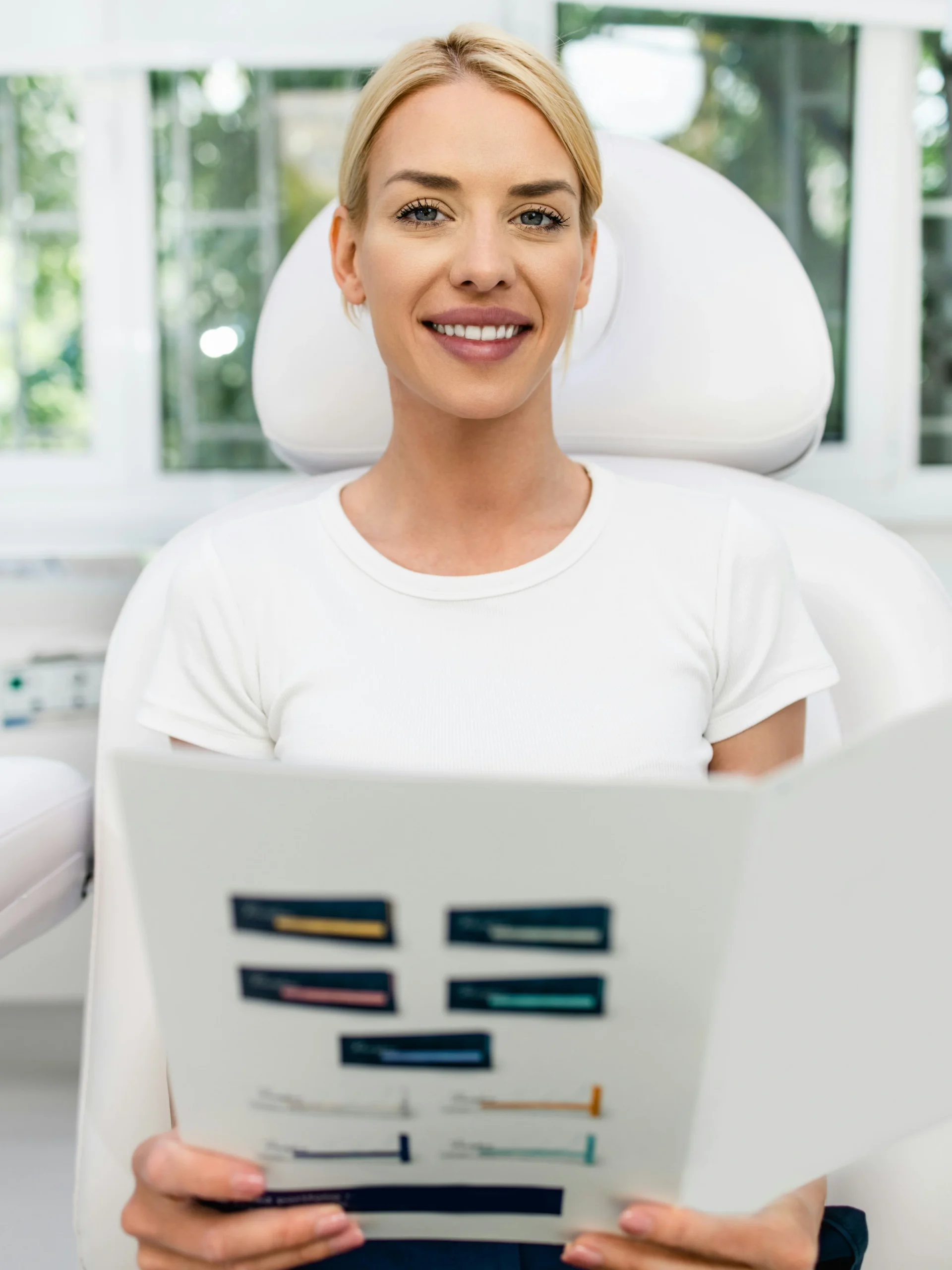 Une cliente assise dans une clinique lumineuse et propre, souriante, tenant un livret d'information sur les soins du visage