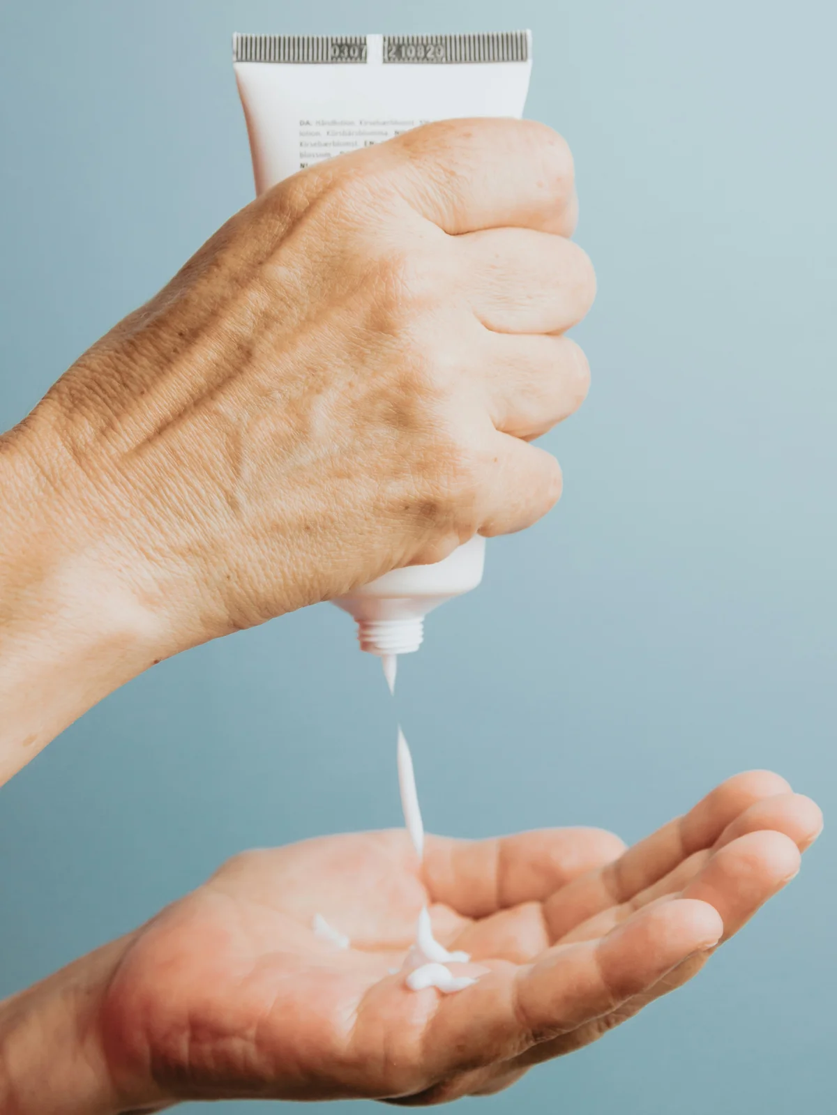 Gros plan sur une main tenant un tube de crème hydratante blanche à la verticale et en déposant un peu dans l'autre main, en dessous