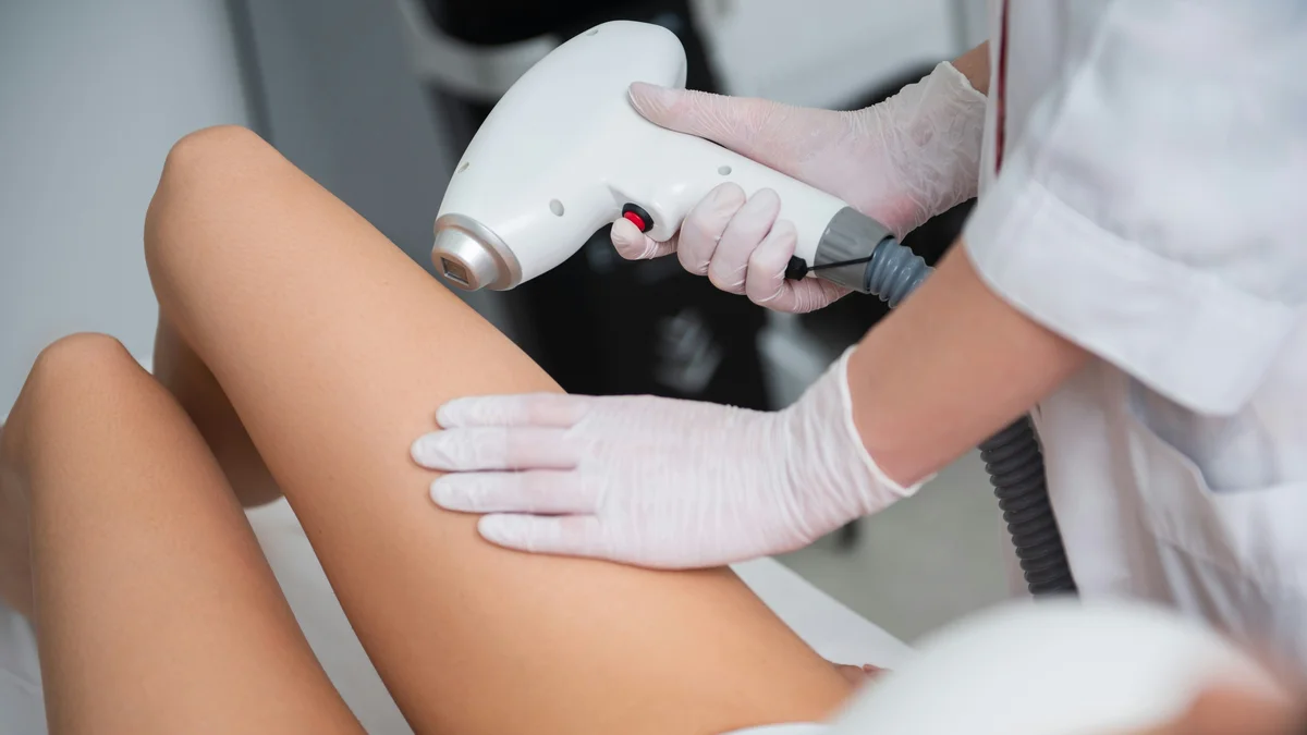 Gros plan sur une esthéticienne traitant le bas de la jambe d’une cliente lors d’une séance d’épilation au laser