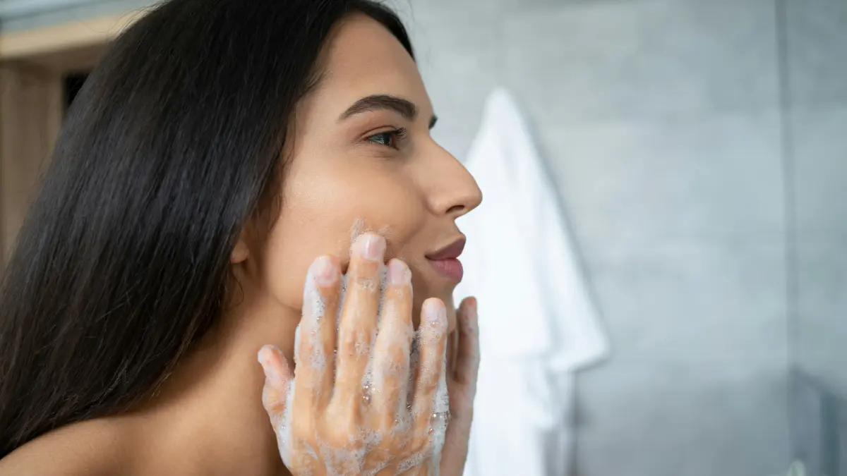 Vue de profil d'une femme qui masse un nettoyant sur son visage, penchée au-dessus du lavabo