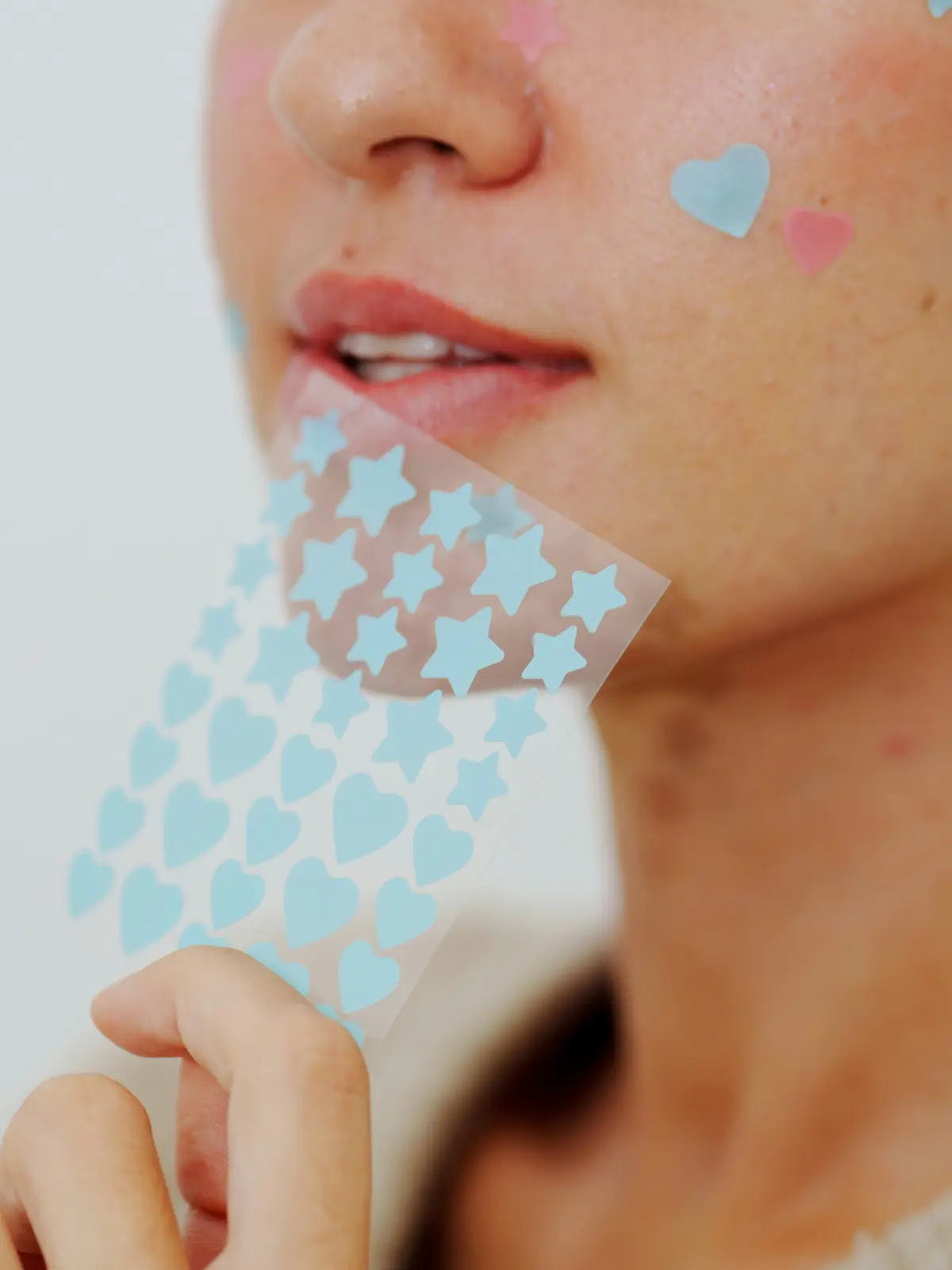Gros plan sur le visage d'une femme portant quelques patchs hydrocolloïdes en forme de cœur et d'étoile sur ses boutons