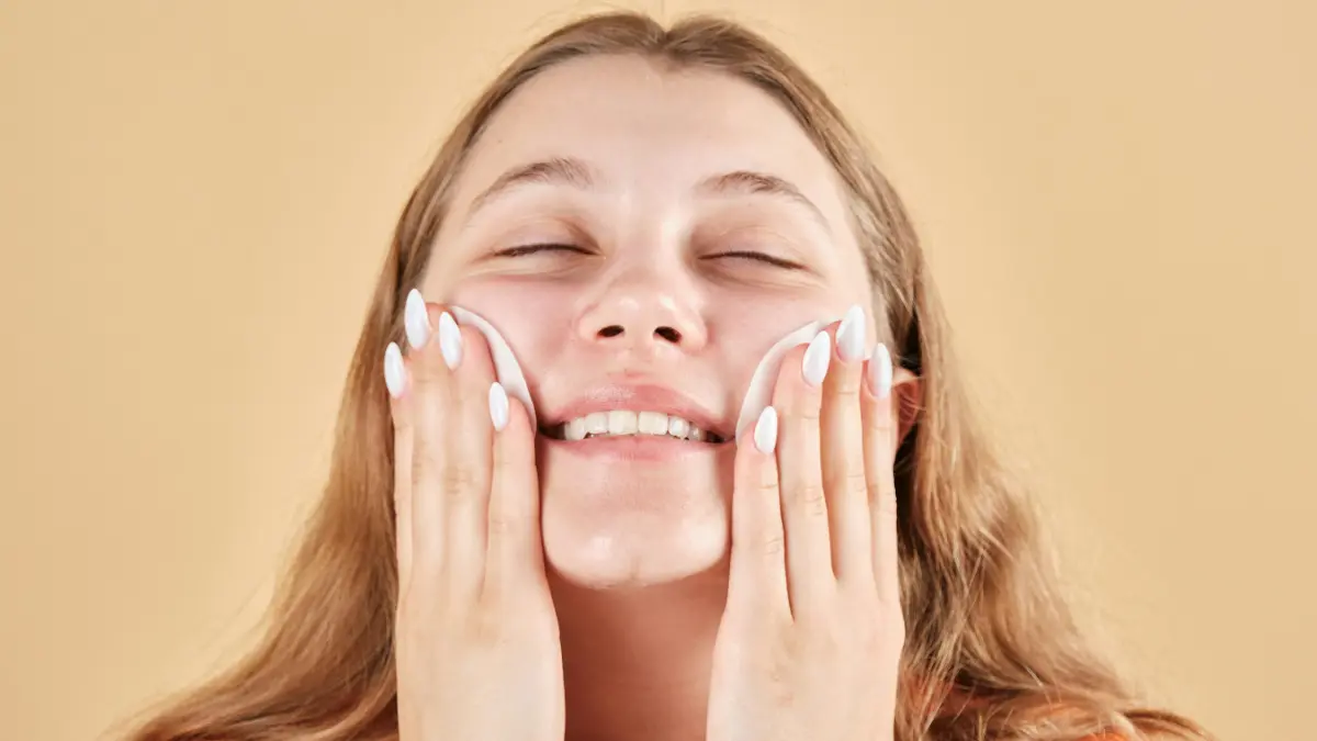 Gros plan d'une jeune femme souriante, les yeux fermés, qui essuie délicatement ses joues avec des cotons