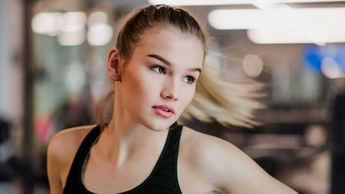 Une jeune femme en débardeur de sport se déplace sur le côté, sa queue-de-cheval volant sur le côté
