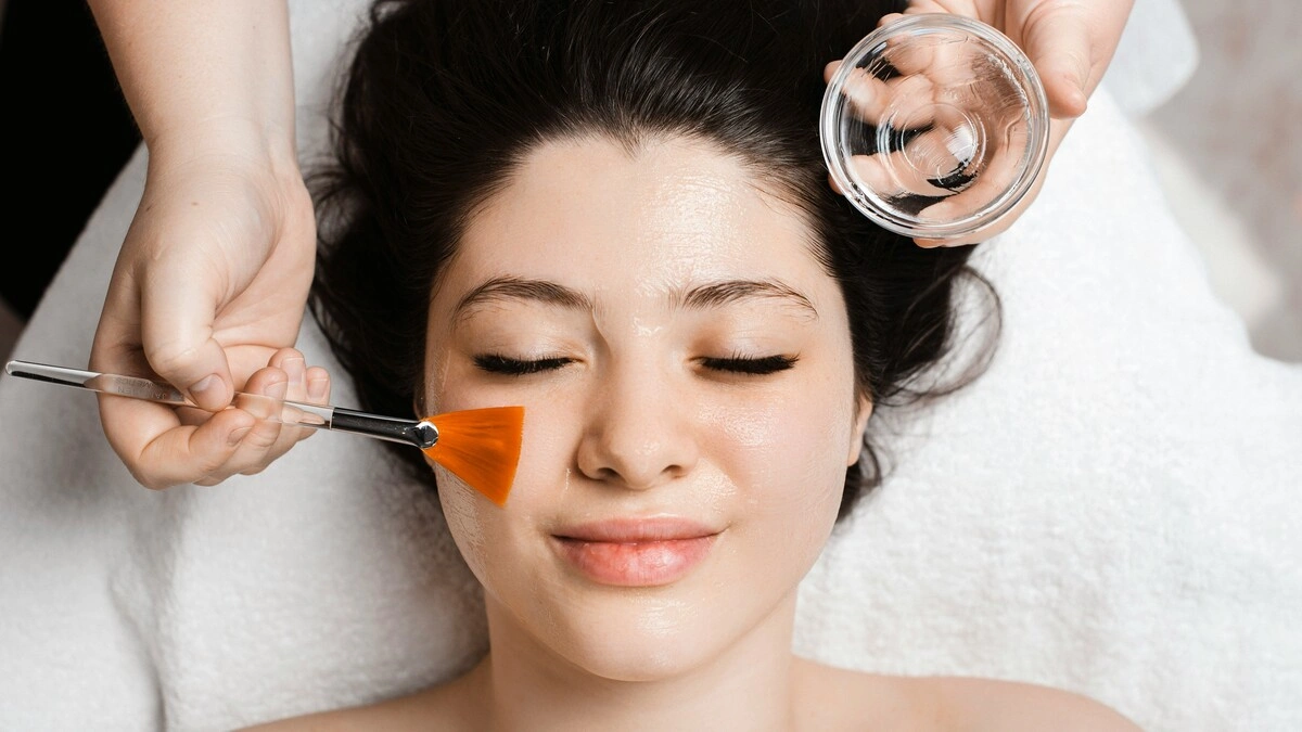 Vue de dessus d'une esthéticienne appliquant une solution de peeling chimique sur le visage d'une cliente à l'aide d'un large pinceau plat