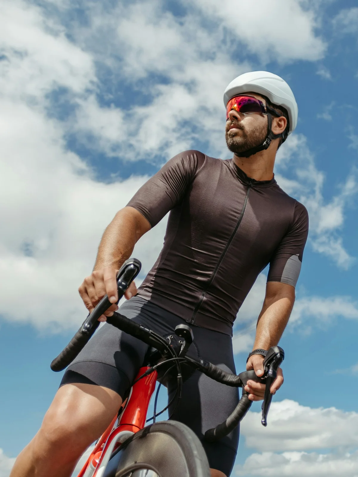 En contre-plongée, un cycliste à califourchon sur son vélo s’arrête pour regarder autour de lui sous un ciel bleu parsemé de nuages