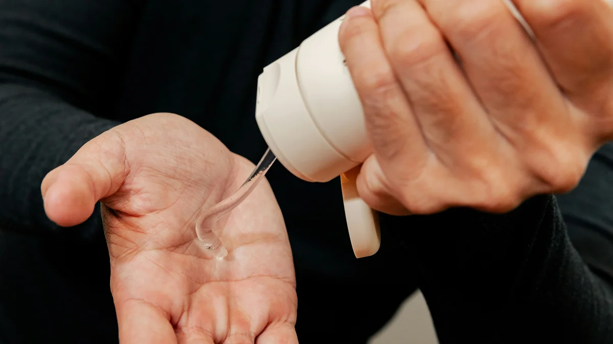 Gros plan sur les mains d’un homme qui presse d’une main un tube blanc de gel hydratant dans sa paume