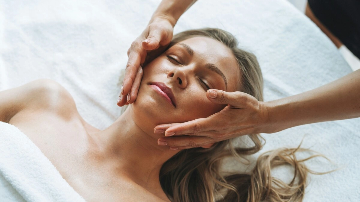 Femme détendue pendant un drainage lymphatique du visage, les mains du praticien glissant délicatement sur ses joues