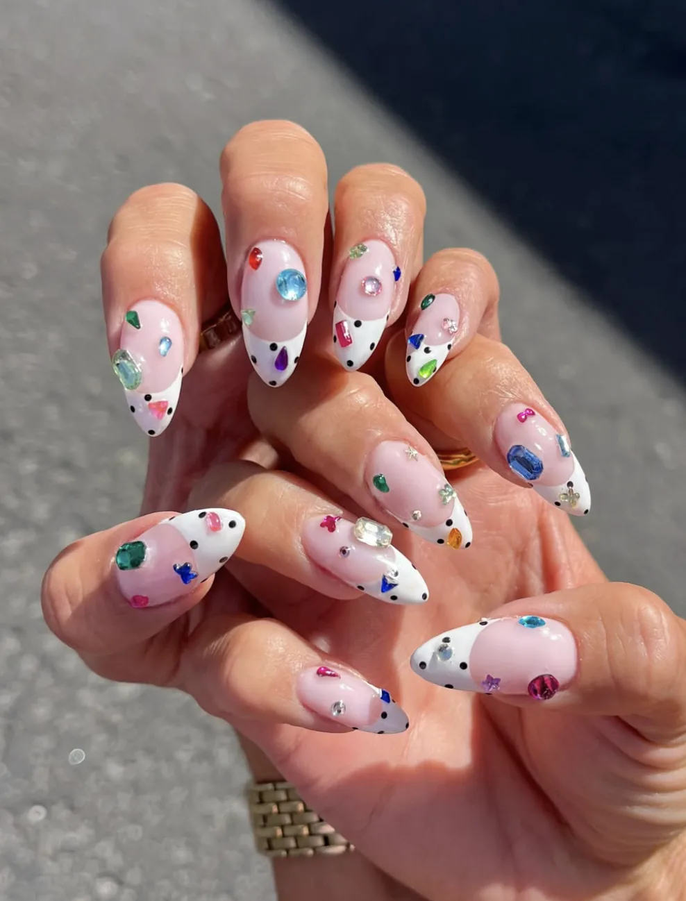 Ongles en amande façon bedazzled avec strass colorés et pointes blanches à pois