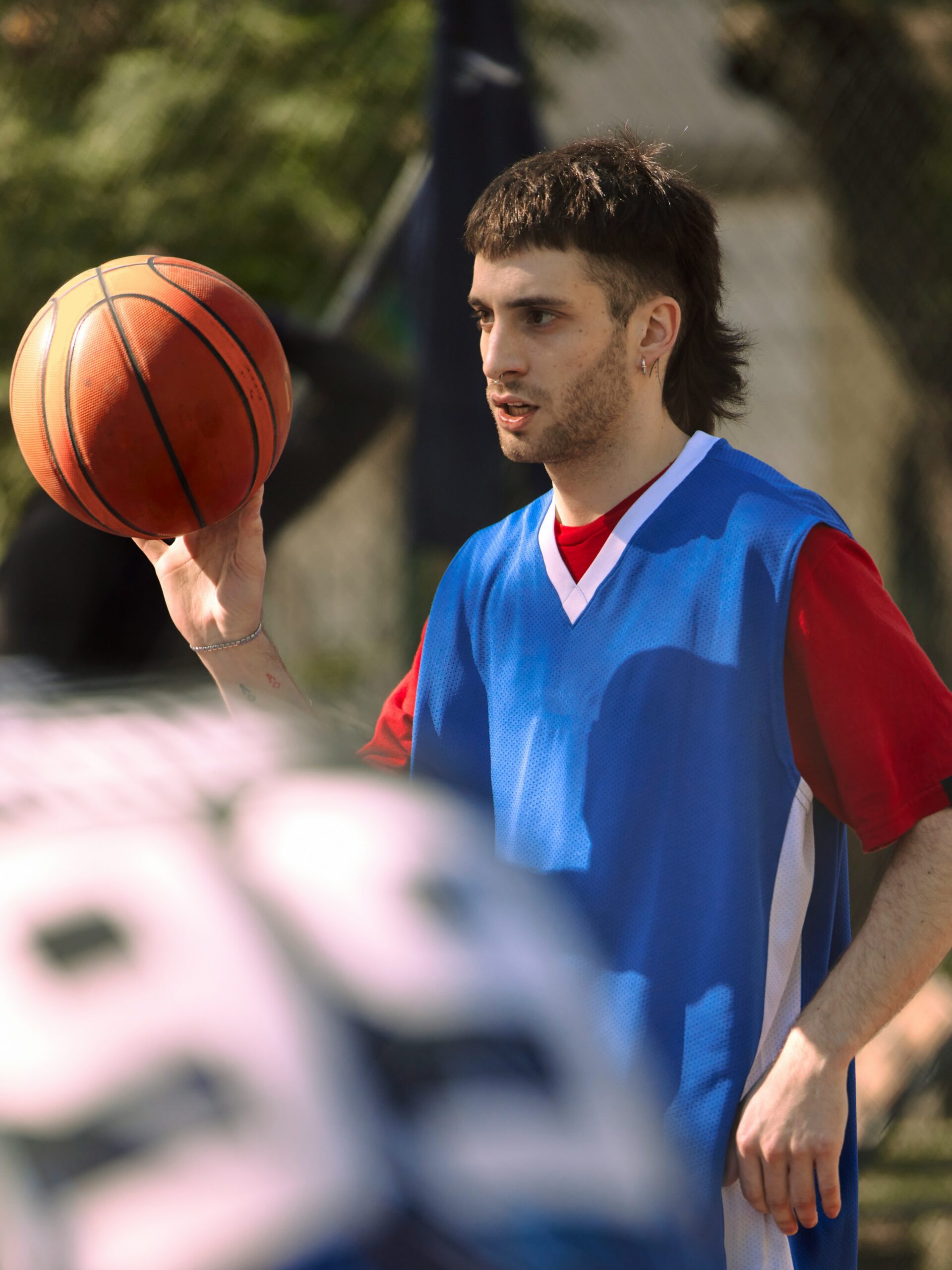 Een jonge man met een fade-mullet-kapsel aan het basketballen.