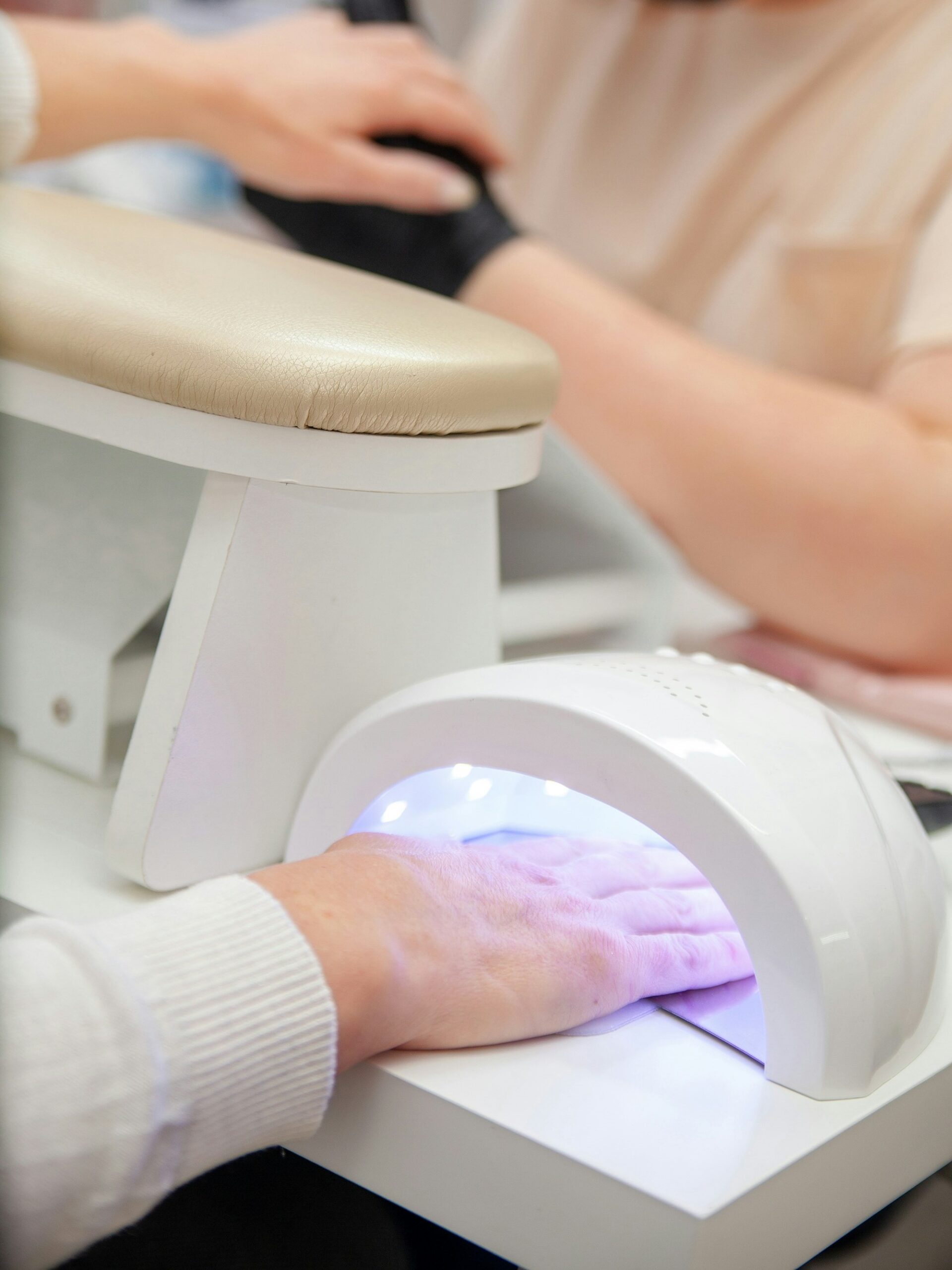 Een klant in een nagelsalon die haar BIAB-manicure laat uitharden onder een UV-lamp