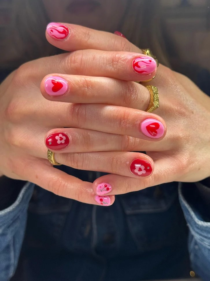 Vrouwenhanden tegen elkaar met een felroze en rode BIAB-manicure met nail art