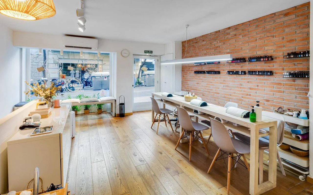 Een hedendaagse salon met een rustieke toets, met een lange witte manicurebar en een rode bakstenen accentmuur. Grote ramen kijken uit op een stadsstraat en vullen de ruimte met houten vloer met natuurlijk licht.