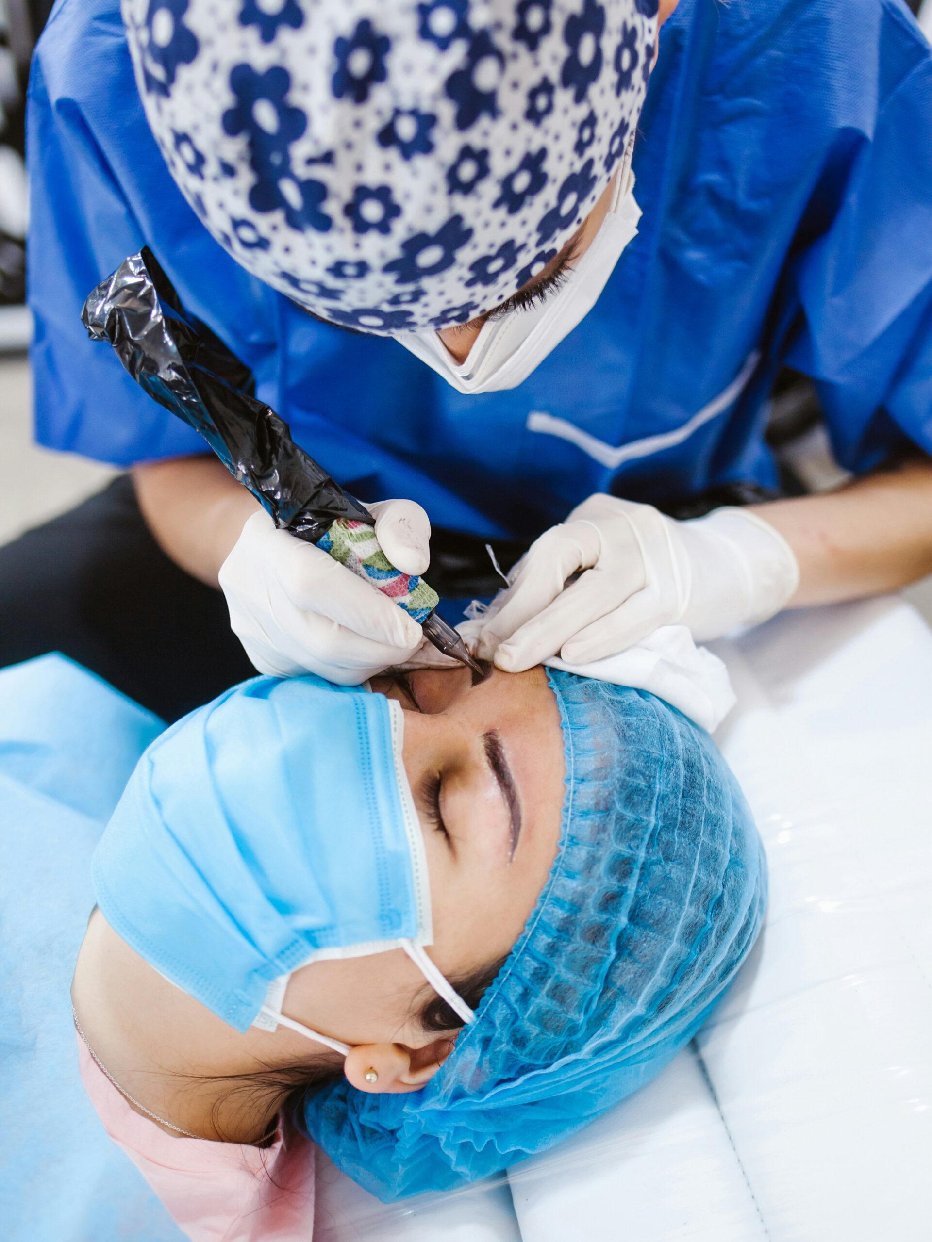 Close-up van een vrouw die een microbladingbehandeling ondergaat door een specialist, ze ligt op een behandelbed en draagt een masker