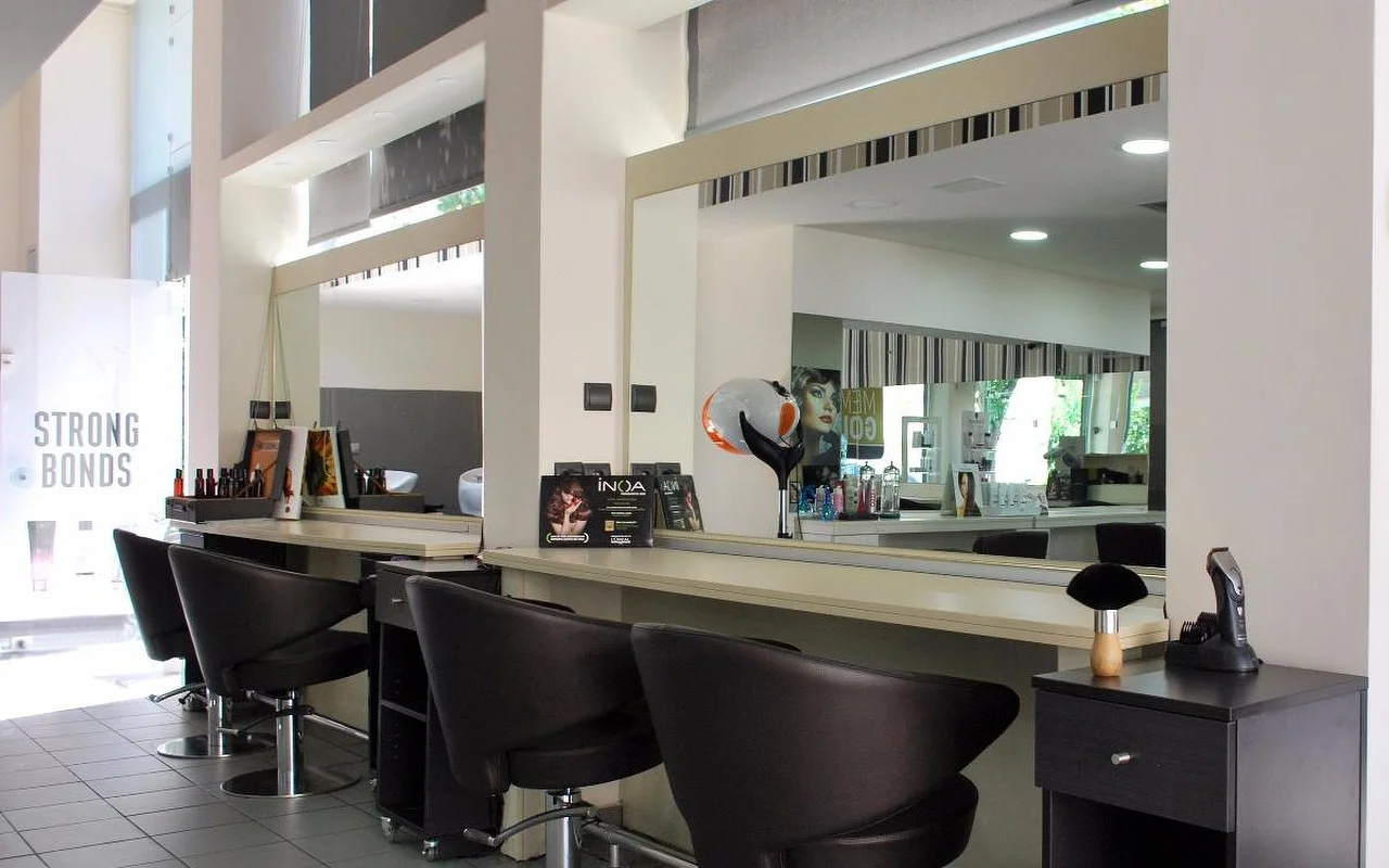 Een professionele haarsalon met donkere leren stylingstoelen tegenover grote spiegels, haarproducten langs de toonbank, hoge plafonds met natuurlijk licht dat door bovenlichten naar binnen valt.