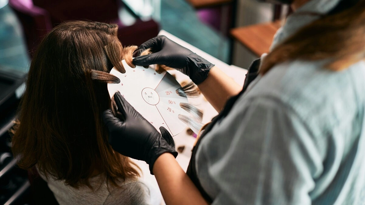 Close-up van een colorist die haarstalen tegen het hoofd van een klant houdt om de tinten voor een balayage te kiezen
