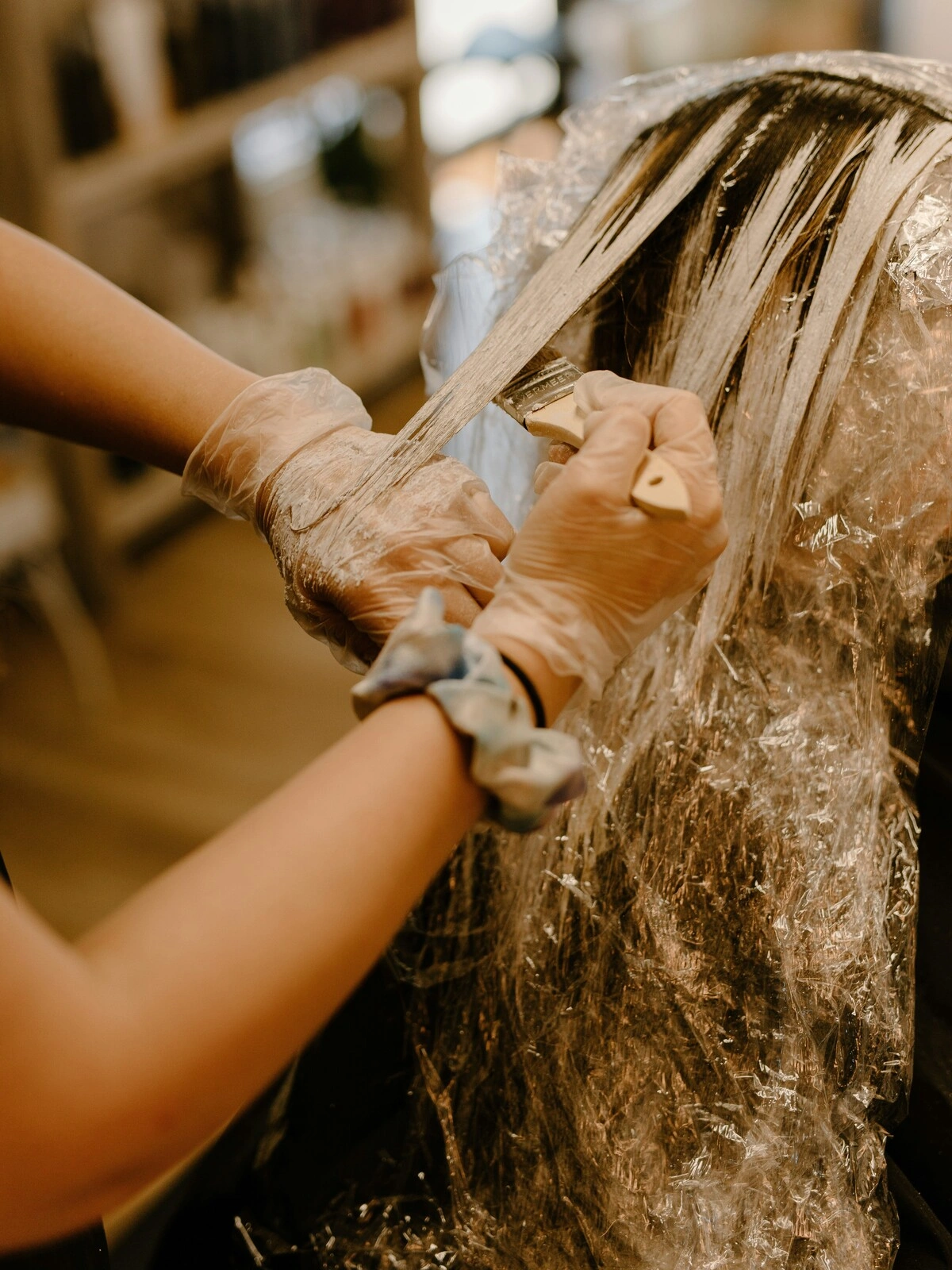 Een colorist met handschoenen brengt met een kwast kleur aan op het haar van een klant, als onderdeel van een balayage