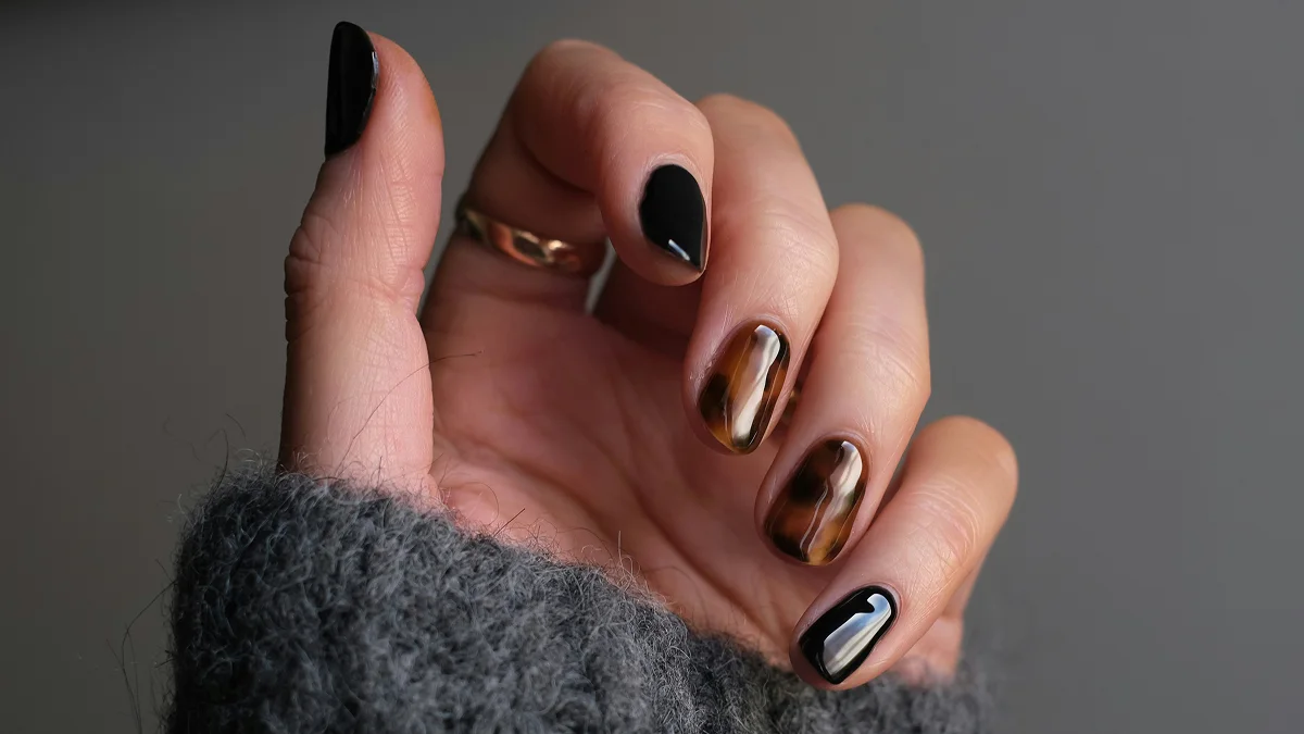 Close-up van een hand met korte nagels en een glanzende gelmanicure in zwart en dierenprint