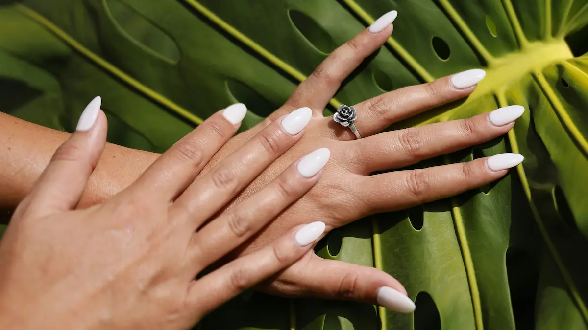Studioshot van verse acrylnagels in amandelvorm met een nudekleur, tegen een achtergrond van palmbladeren