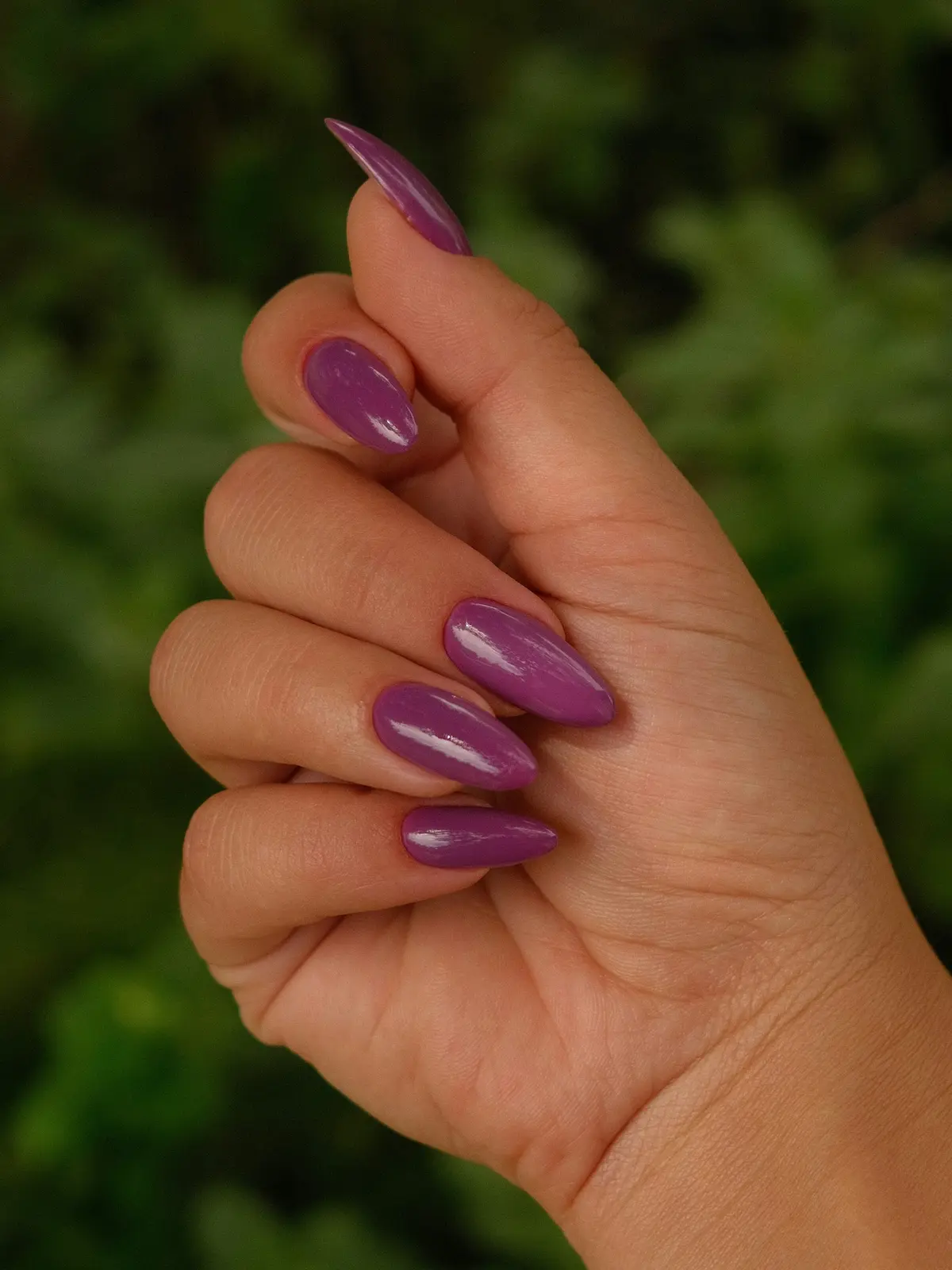 Close-up van de hand van een vrouw met paarse acrylnagels in amandelvorm
