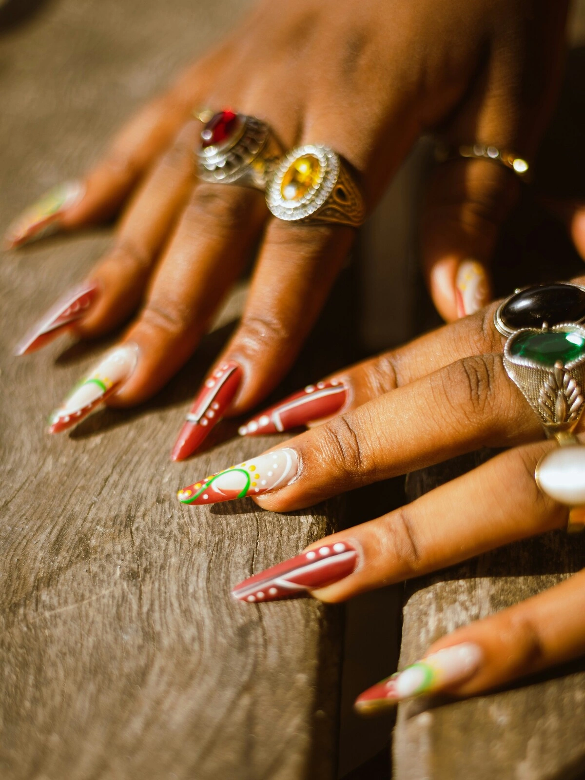 Close-up van de handen van een vrouw met stilettovormige acrylnagels in rood en wit, versierd met groene en gele stippen en krullen
