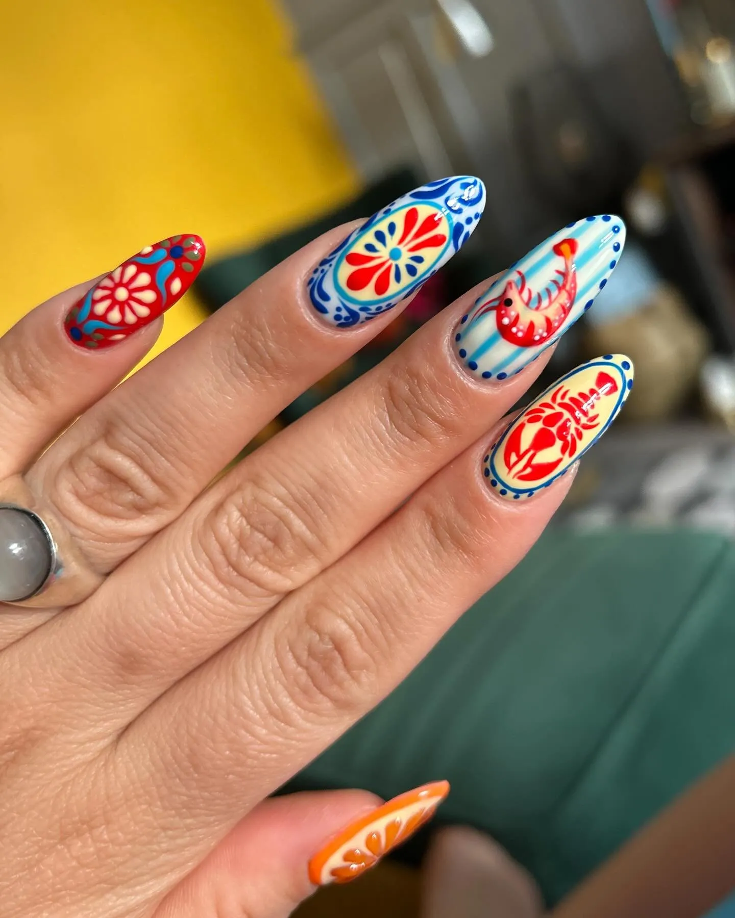 Destination nail art op amandelvormige nagels met mediterraan geïnspireerde motieven in rood, blauw en oranje